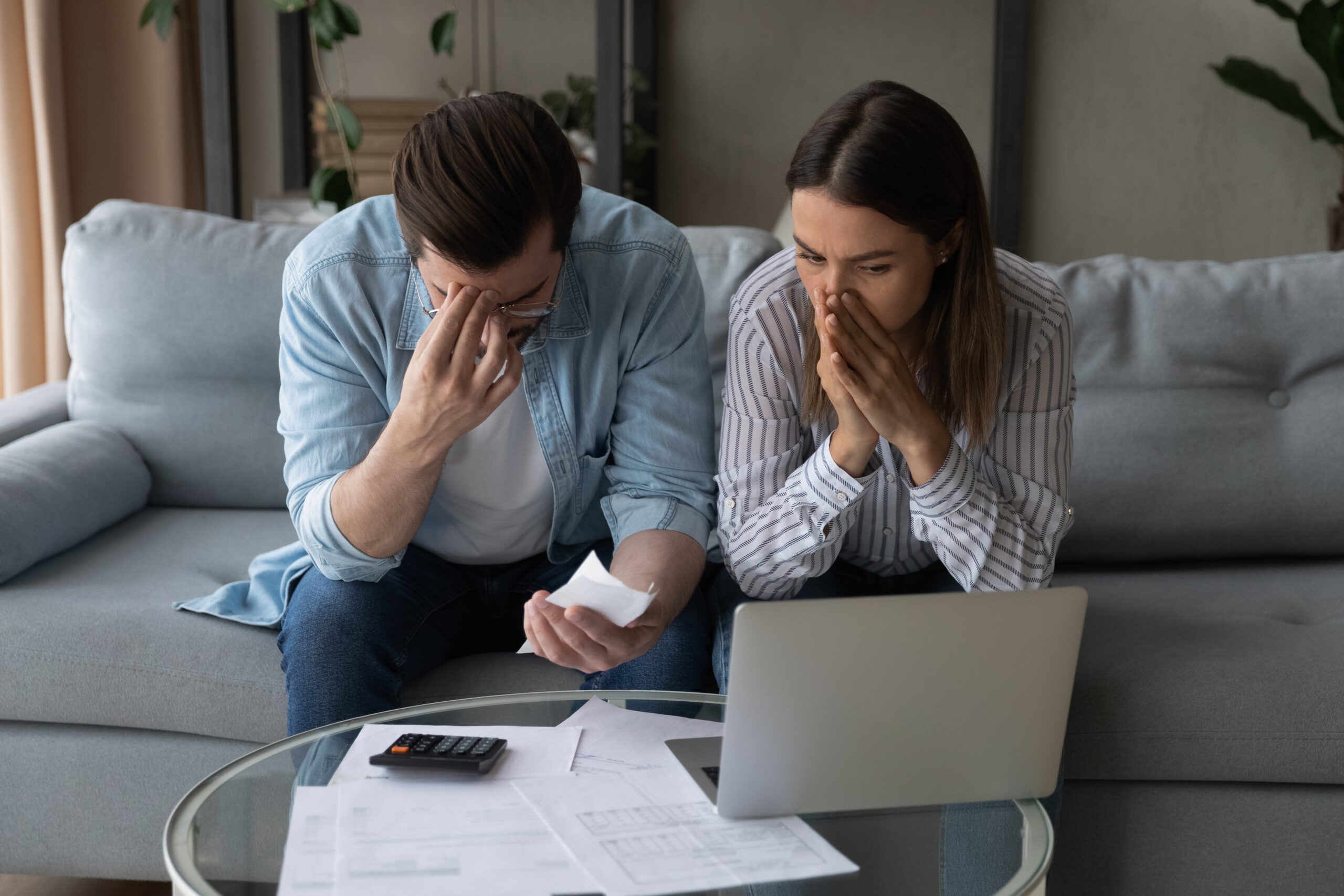 confused and upset couple on couch with laptop