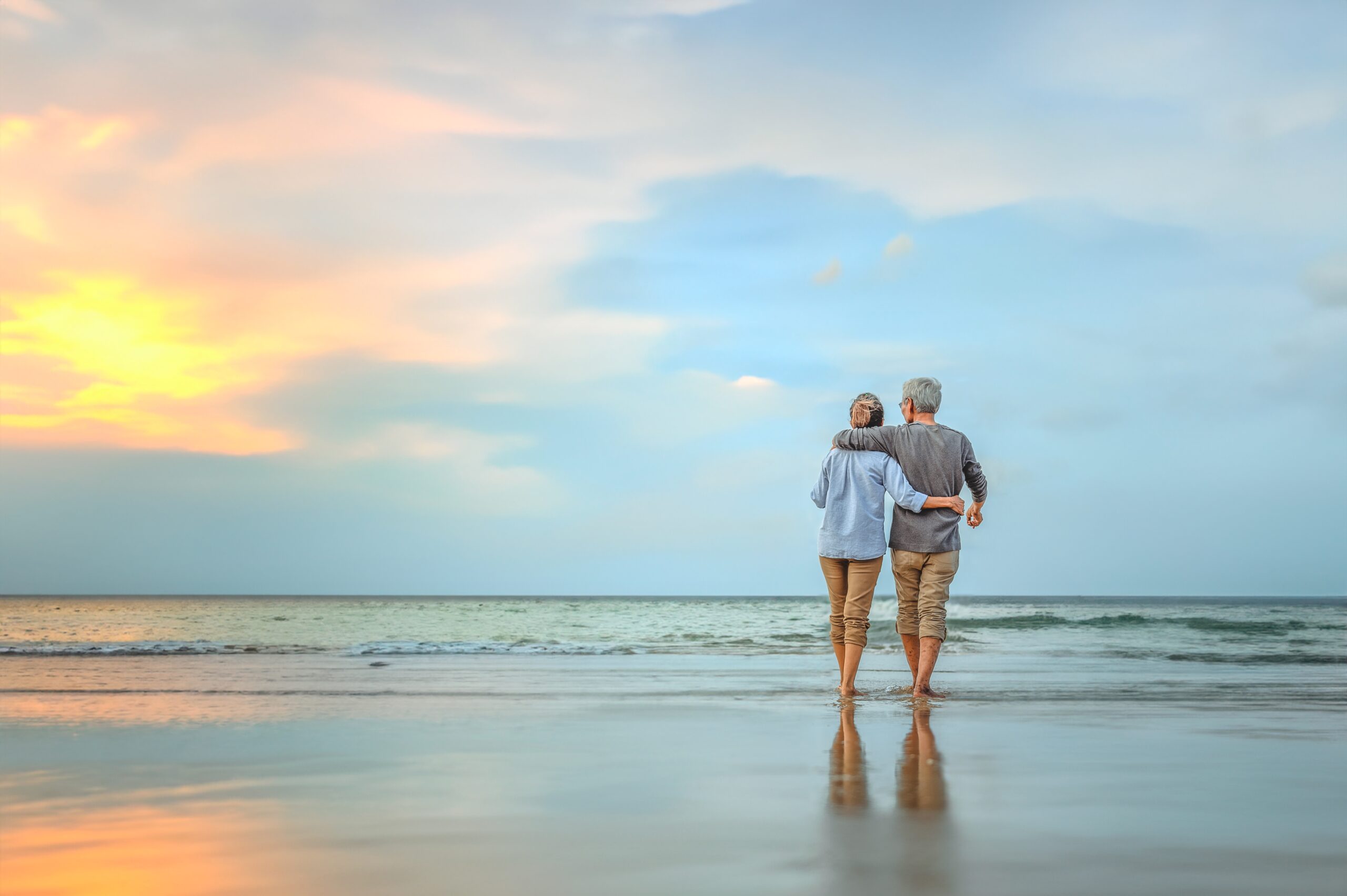 senior couple walking into sunset on beach