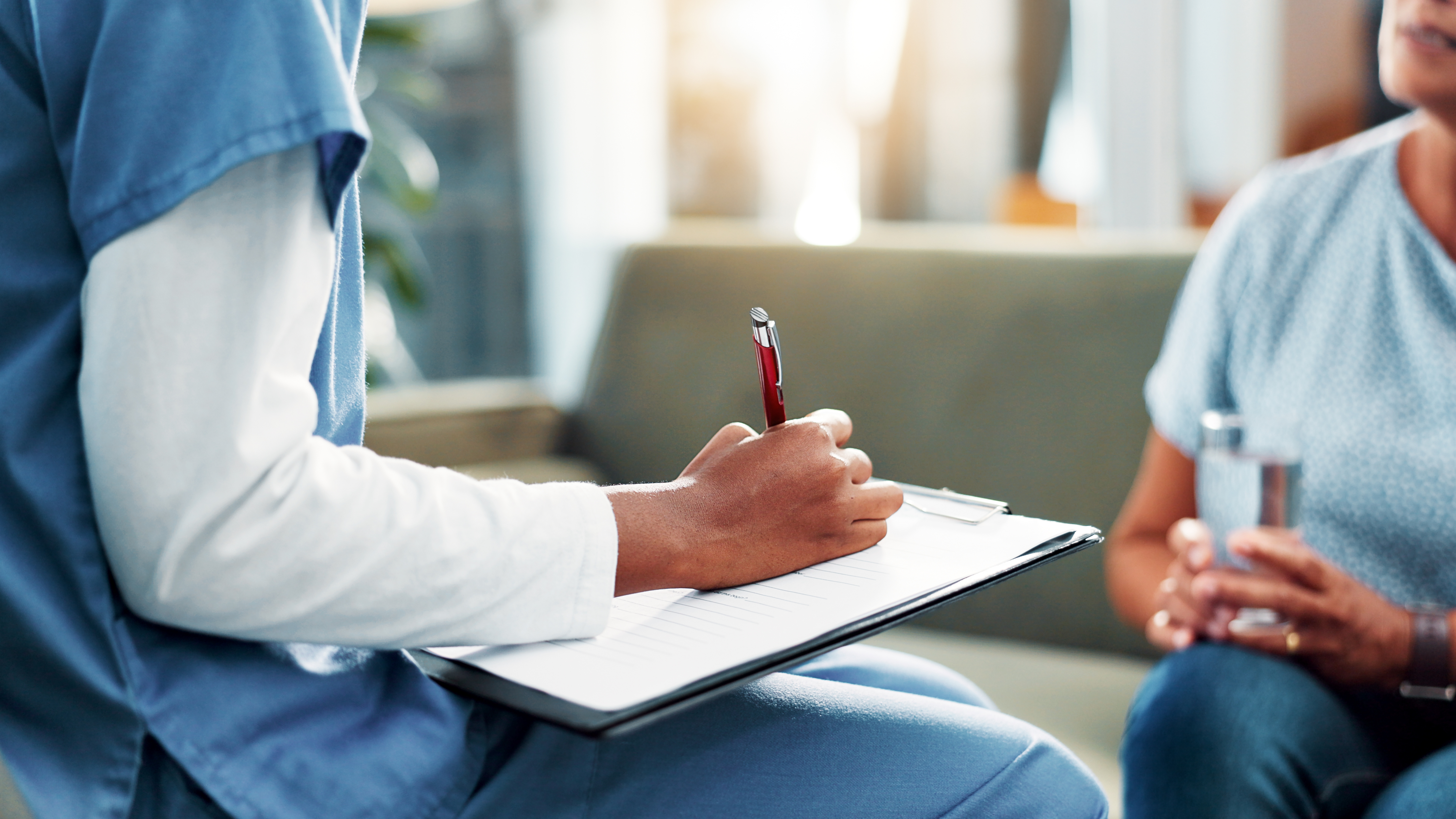 nurse writing on clipboard sitting across from patient