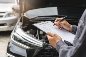 car with hood open and person holding clipboard and writing in front of it