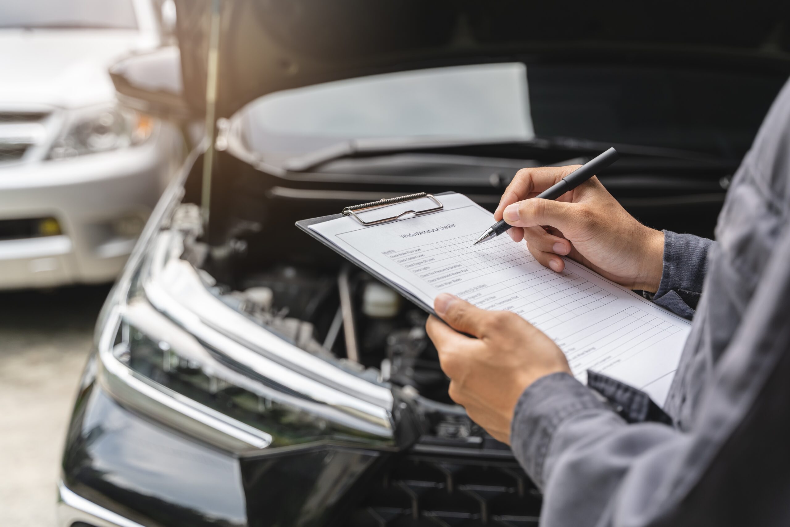 car with hood open and person holding clipboard and writing in front of it