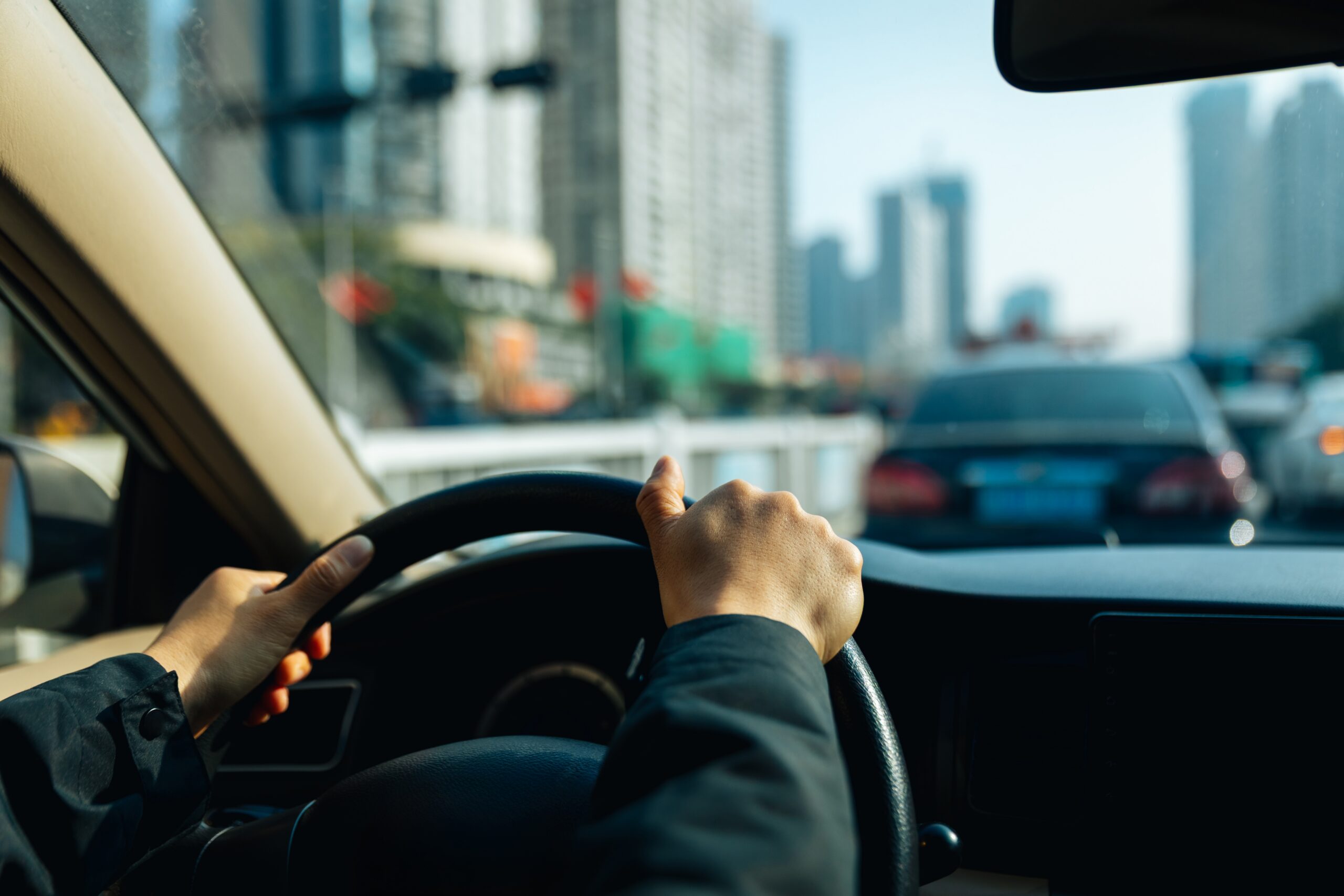 two hands on wheel of car driving in city