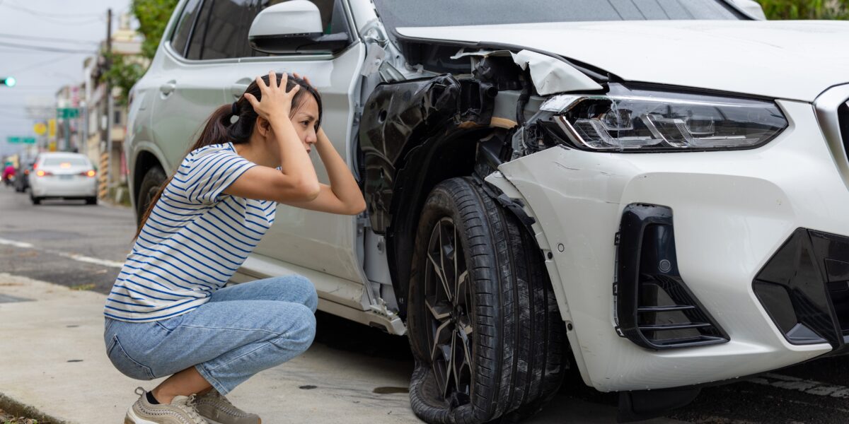 frightened woman sits in front of crashed car