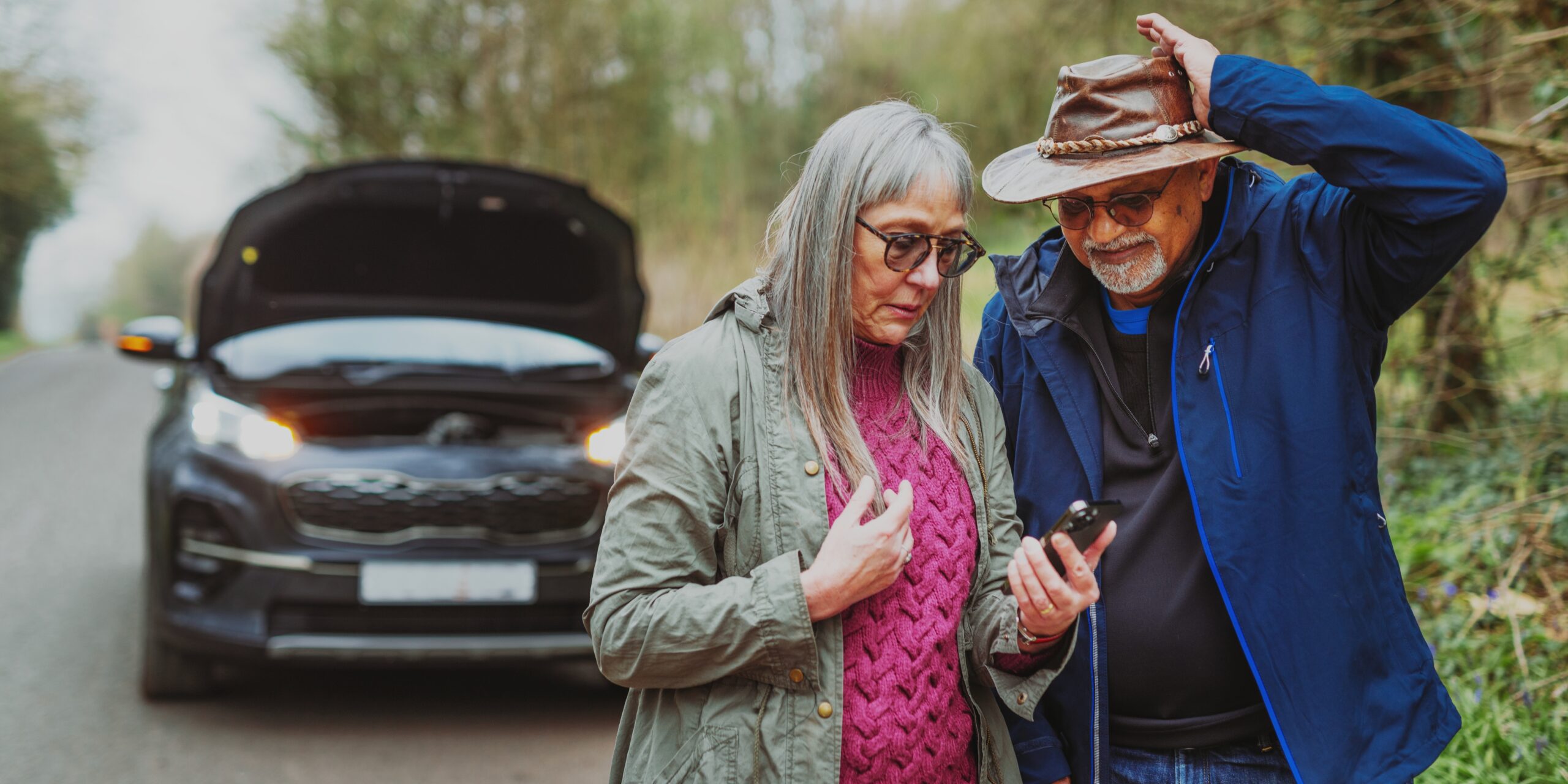 elderly couple standing by car on the phone