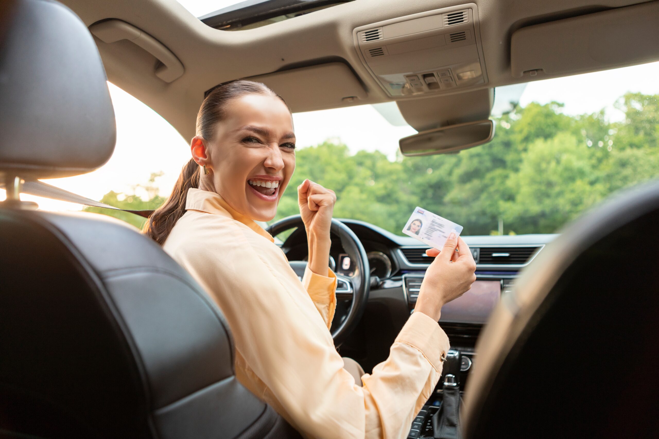 overjoyed young woman in car holding license