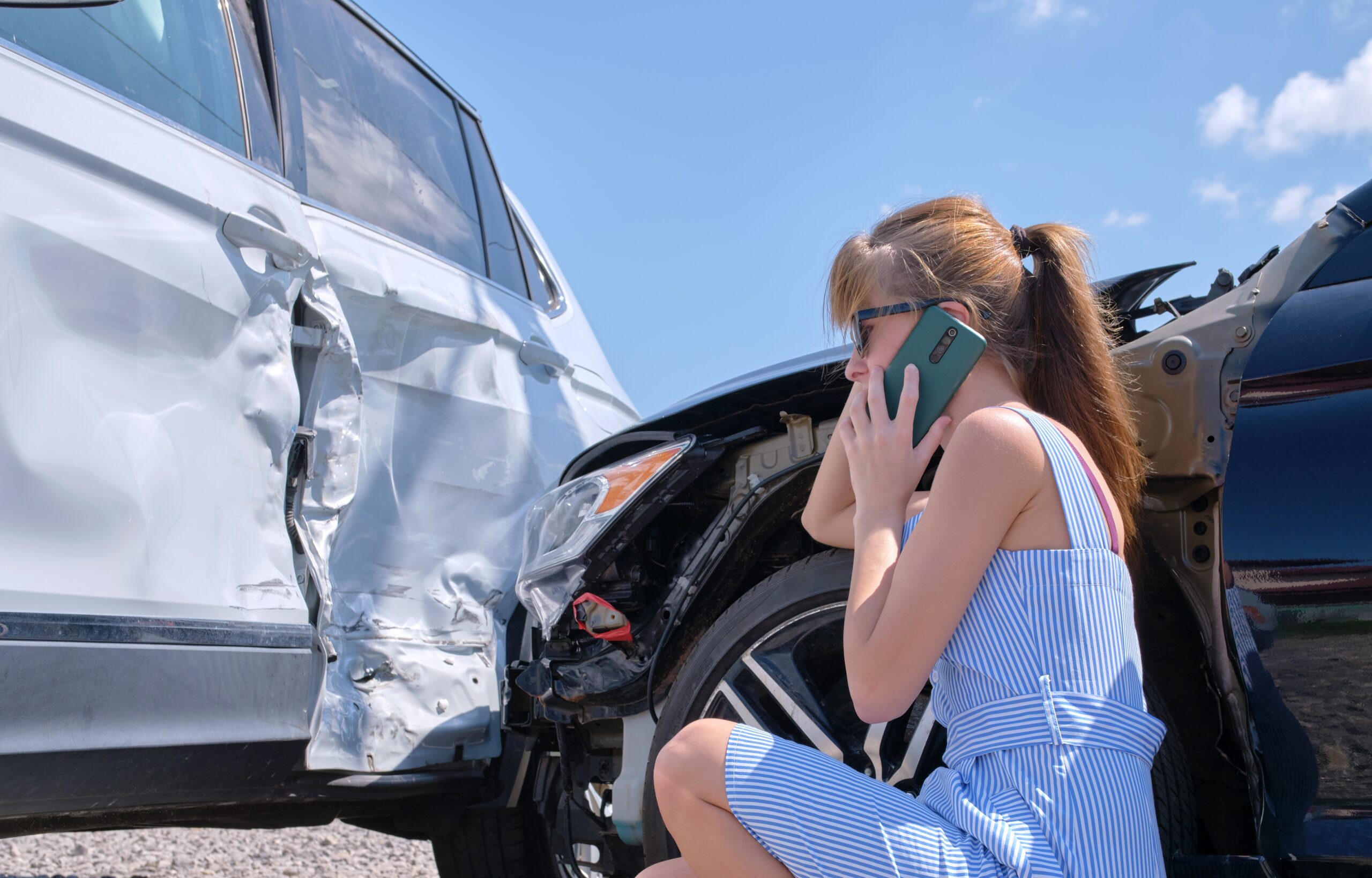 female driver next to wrecked car on the phone