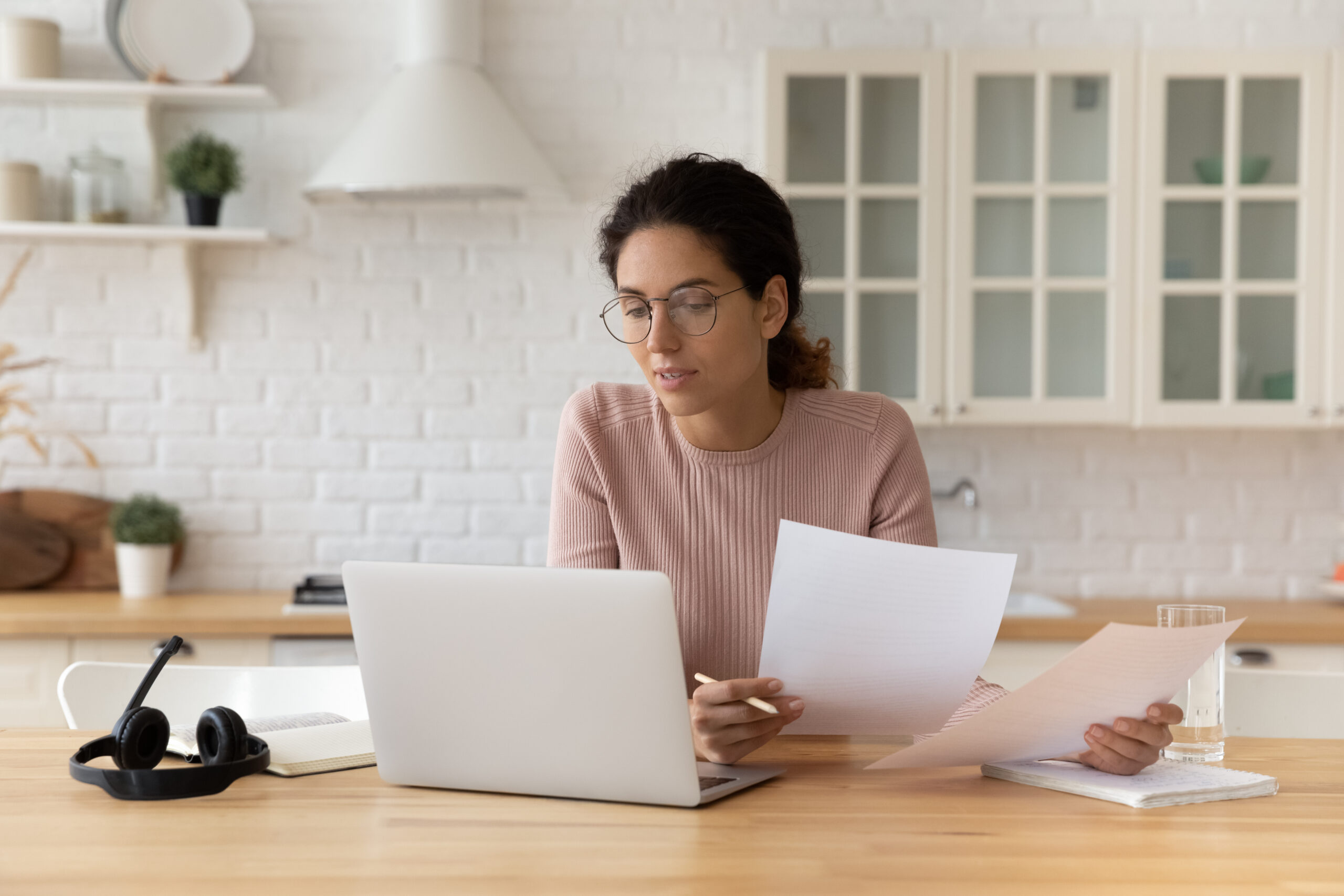thoughtful hispanic female at home on her laptop and holding papers