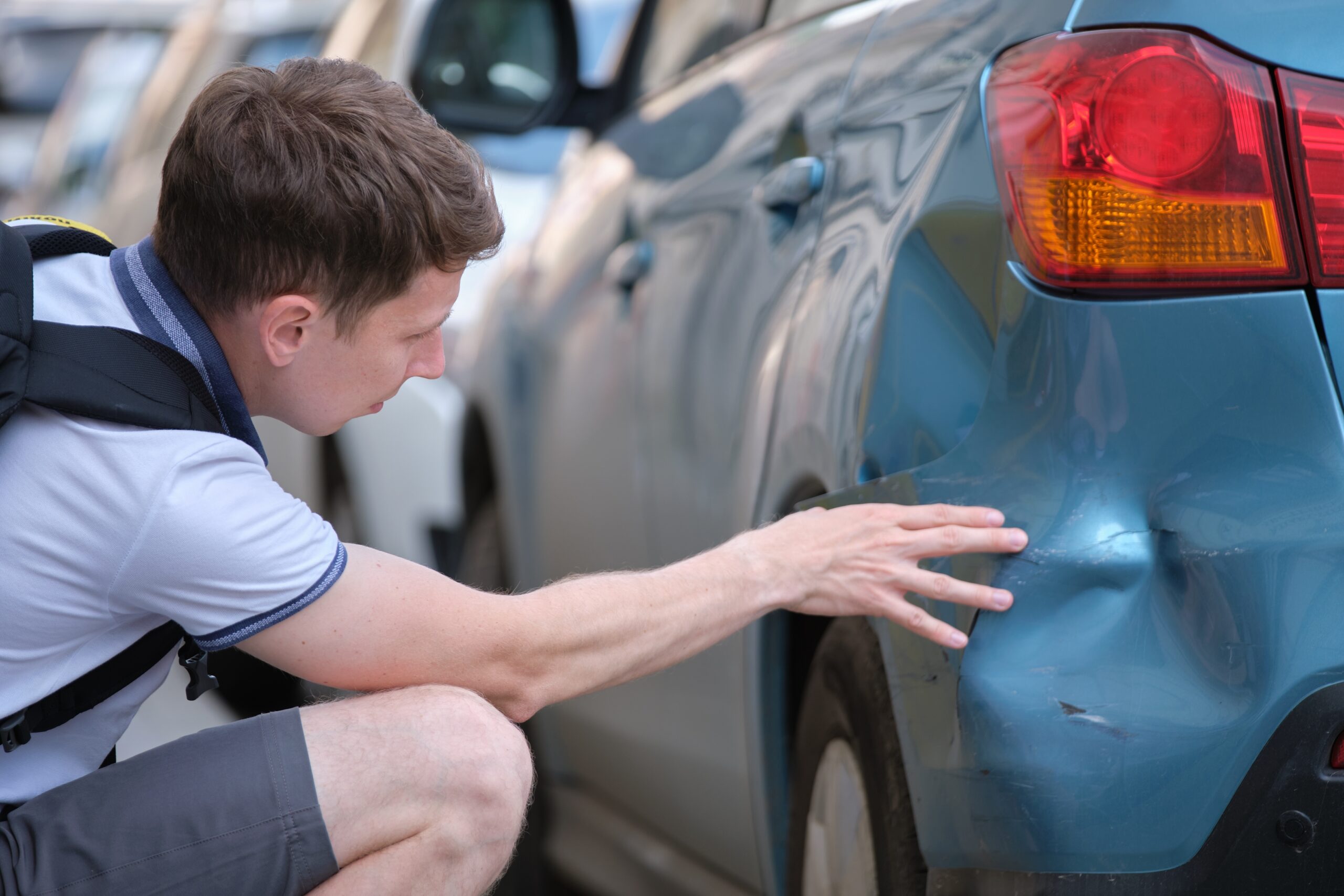 male sitting on street in shock over dent in car