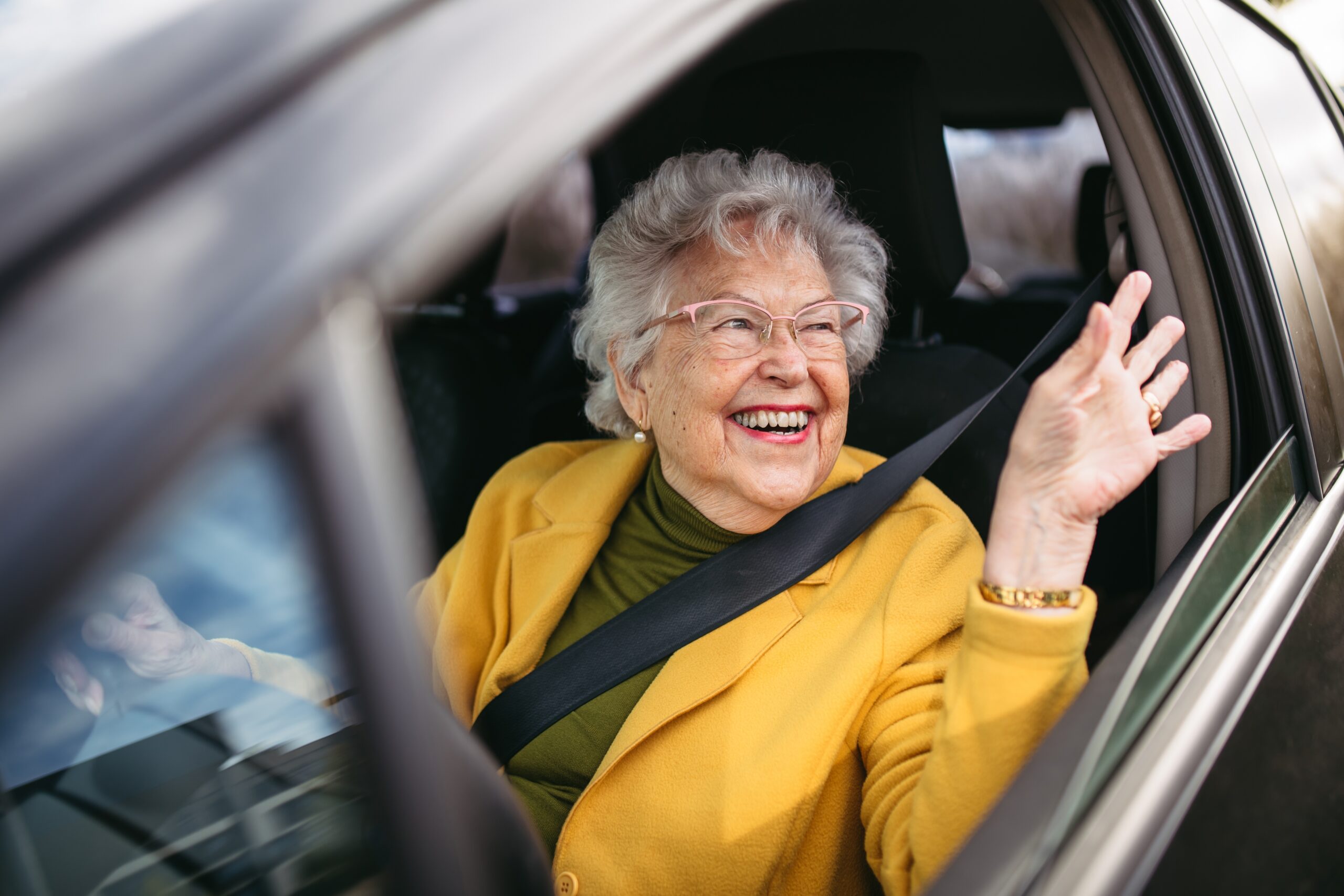 happy elderly woman waving and driving a car